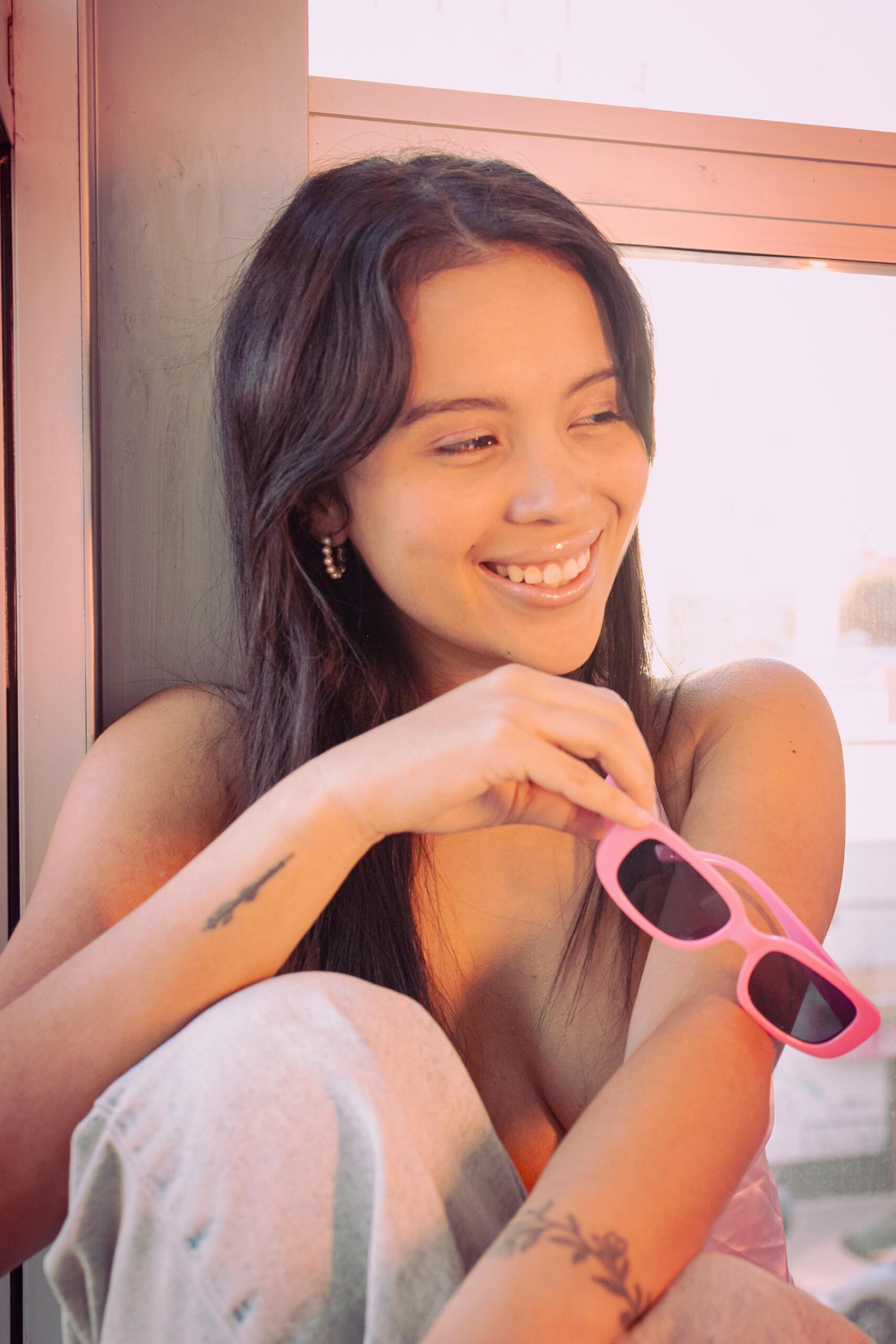 Bright photo of a young woman in Buenos Aires holding pink sunglasses indoors.